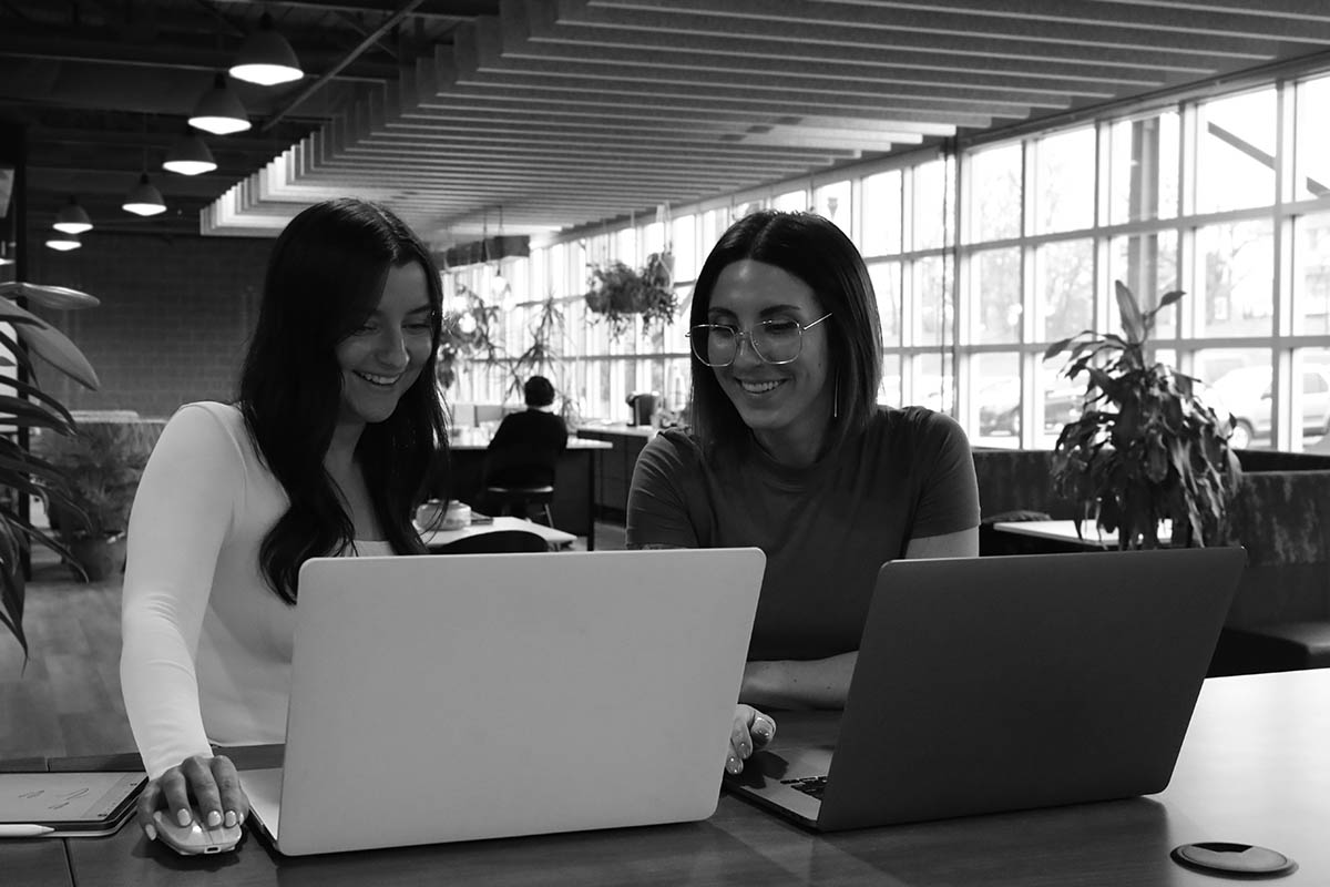 Two women working on laptops smiling 