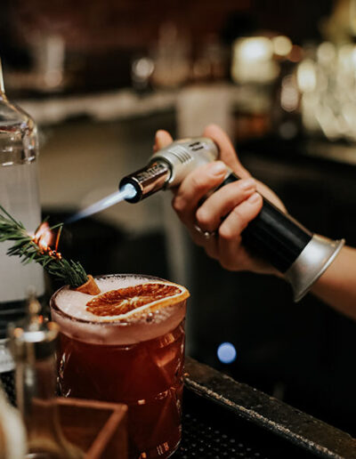hand using torch to smoke a rosemary sprig in a drink
