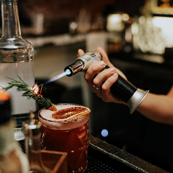 hand using torch to smoke a rosemary sprig in a drink