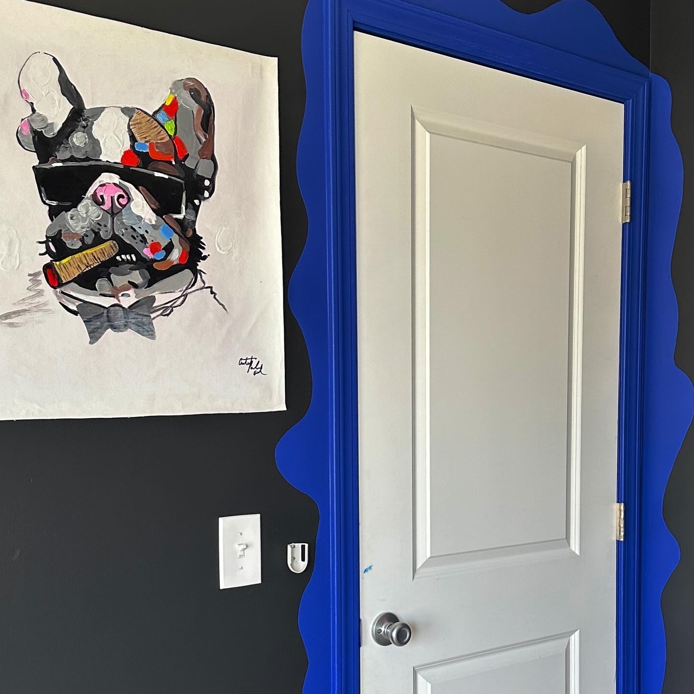 hand painted pug painting with cigar in its mouth and wearing sunglasses, door next to the painting has bright blue wavy paint around it
