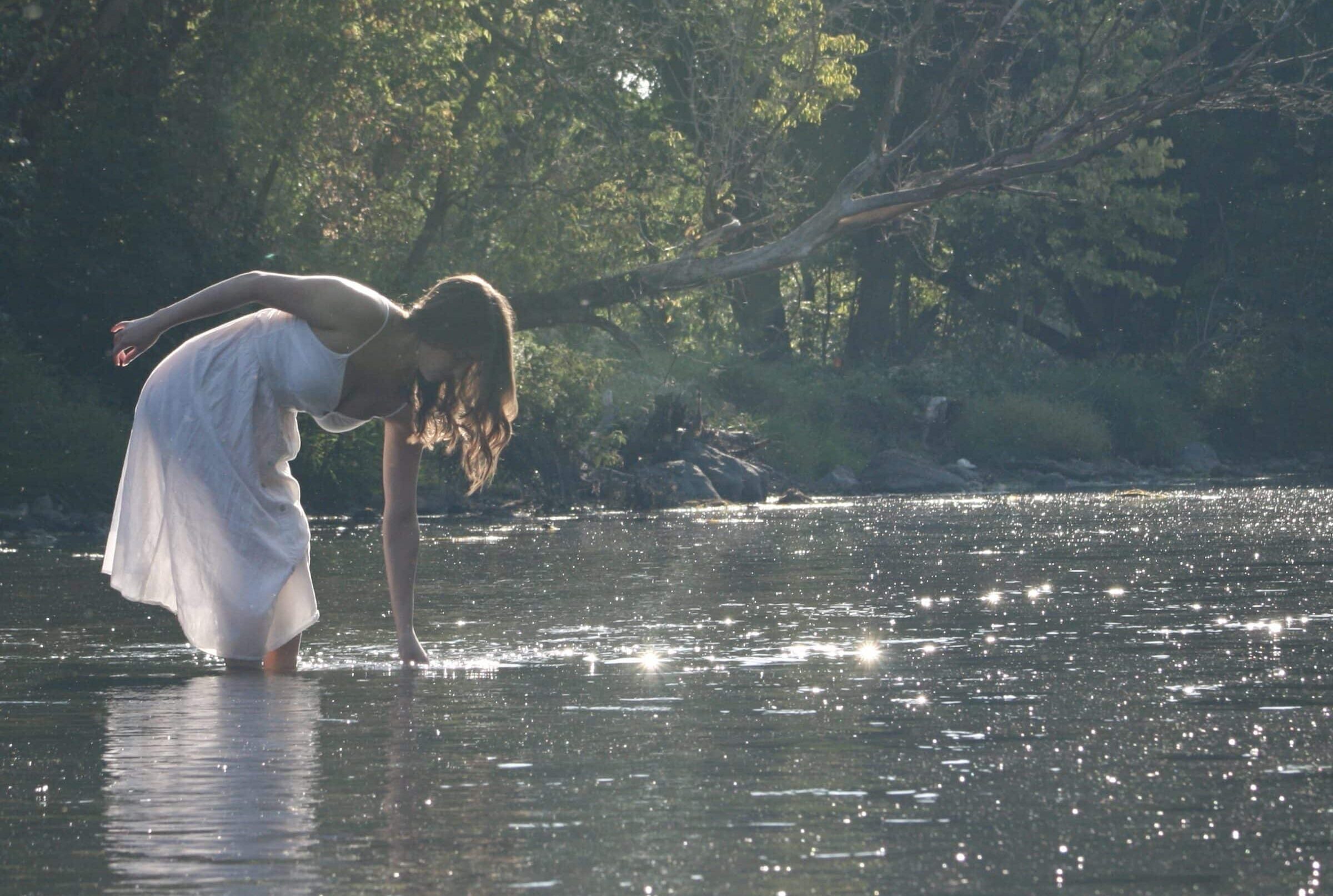 Woman reaching into river with sun reflecting off surface